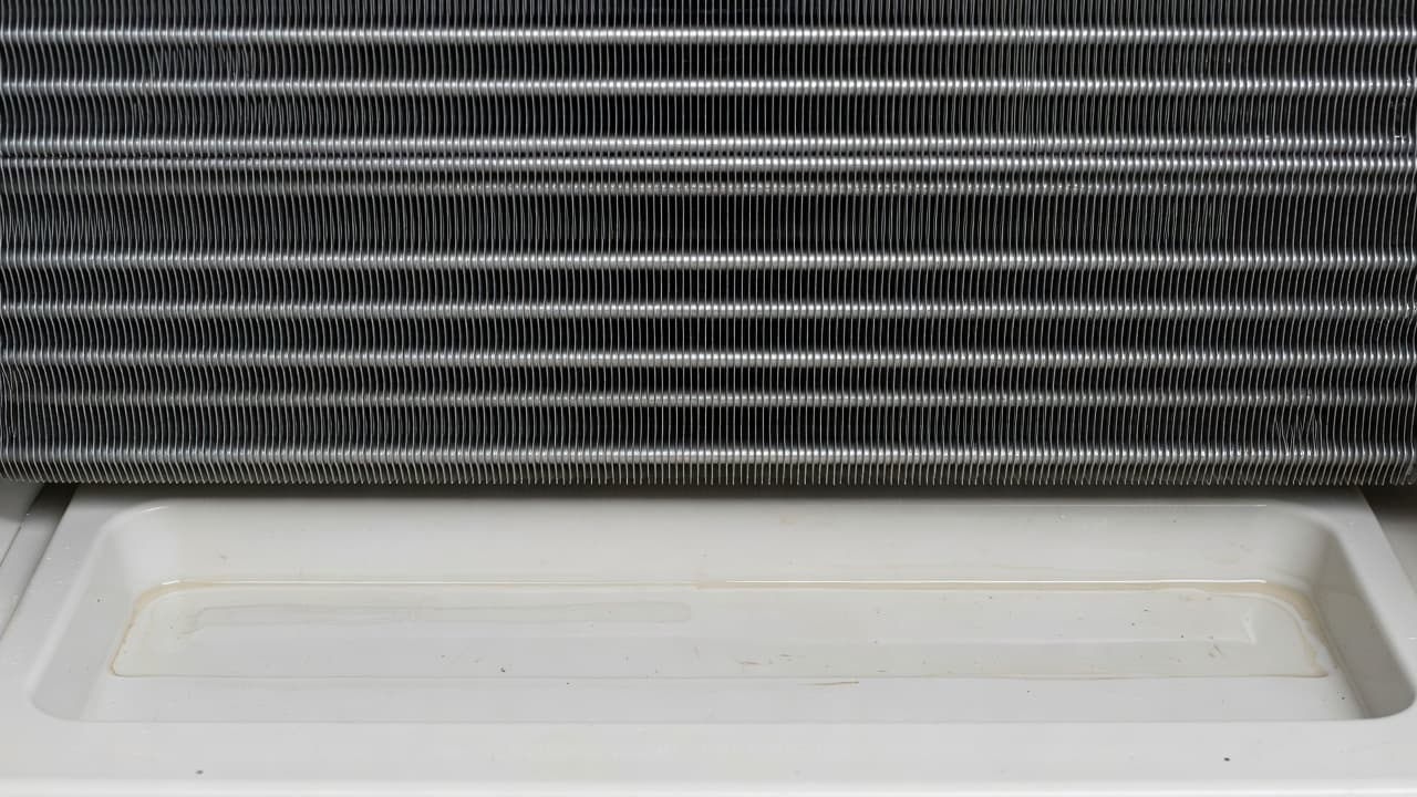 Close up of metal AC coils and a plastic drain pan inside a home air conditioning unit.